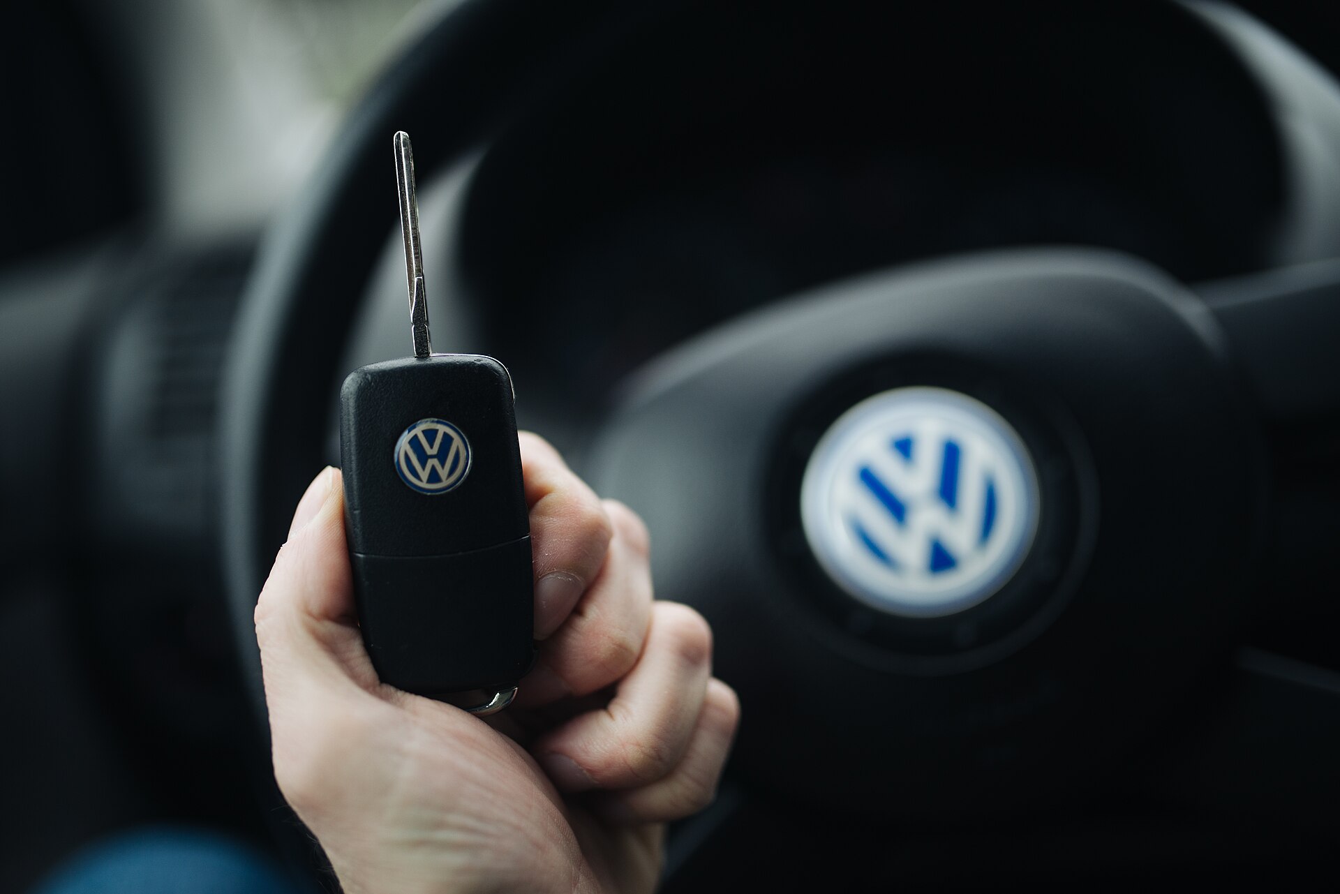 A hand holding car keys, steering wheel in the background